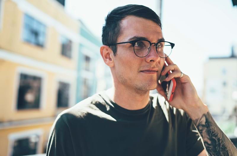 A man wearing glasses talking on the phone outside.